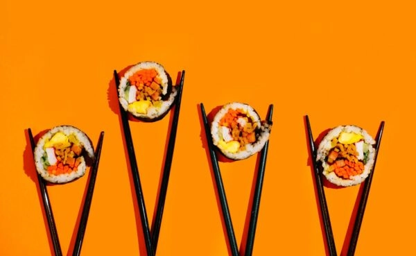 Four colorful sushi rolls held up with chopsticks showcasing Plaza Catering's vibrant and fresh sushi catering menu in Kerala